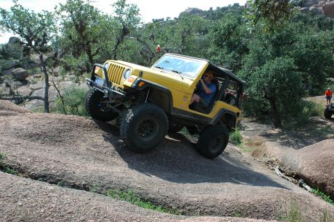 2001 Jeep Wrangler - A yellow 2001 Jeep Wrangler navigates a challenging rocky terrain with another vehicle visible in the background.