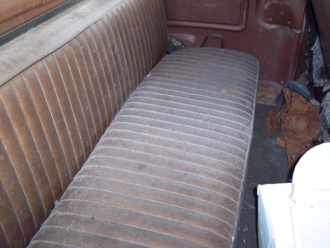 1978 Ford F-250 - Interior view of a brown vinyl bench seat with a ribbed pattern, showing signs of wear and rust in the background.