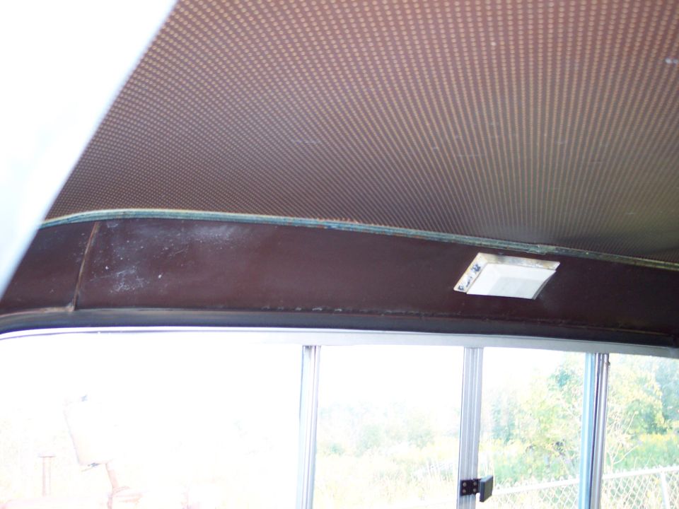 Interior view of a vehicle's headliner and upper dashboard area, showing a patterned headliner and a small light fixture