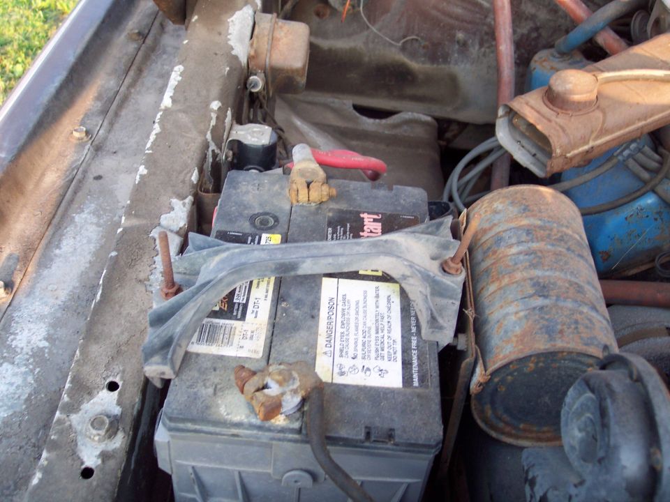 Engine bay showing a car battery, some hoses, and rusty metal components