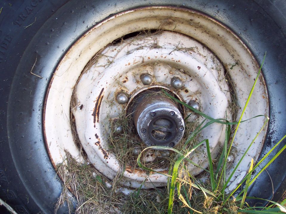 Close-up of a rusty truck wheel hub with grass growing around it