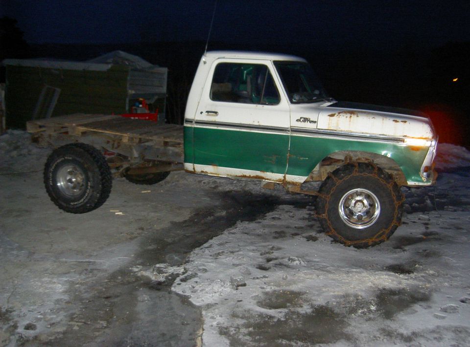 White and green Ford pickup truck with a flatbed, snow chains on front tires