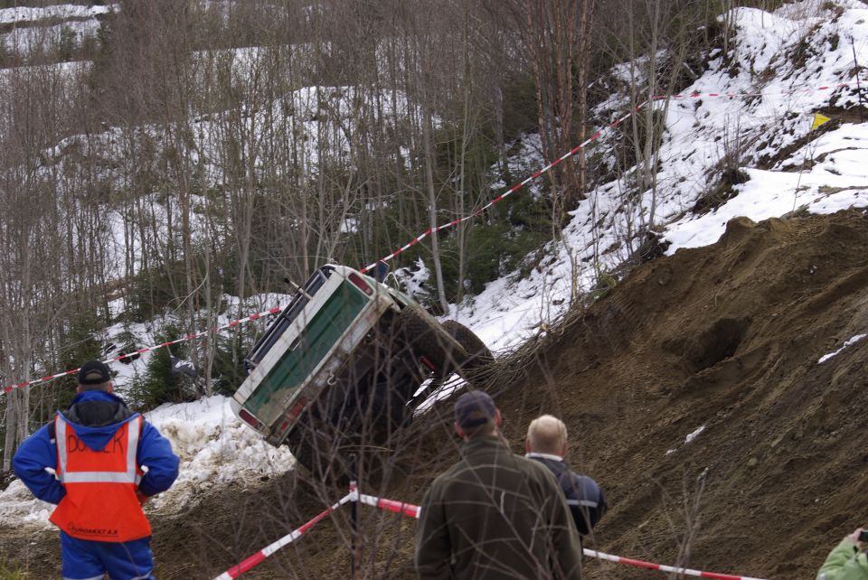 Off-road vehicle tilted on a muddy slope with spectators watching