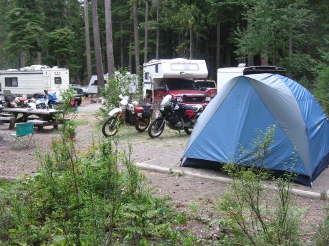 1979 Ford Bronco - A campsite scene two dirt bikes, RVs, and a tent among trees.