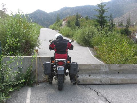 1979 Ford Bronco - A motorcycle is blocked by a concrete barrier on a road surrounded by vegetation and mountains.