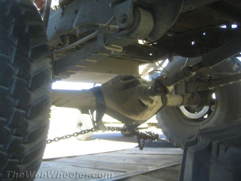 1990 Ford Bronco - Low-angle underside view of an off-road truck's rear solid axle, leaf springs and shock absorber while chained to a trailer.