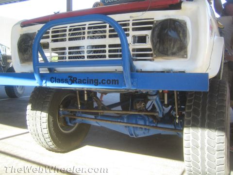 1990 Ford Bronco - Close-up of a white early Ford off-road race truck's front end with a blue tube bumper marked Class3Racing.com over an exposed solid axle.