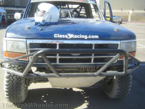 1990 Ford Bronco - Front end of a blue Ford off-road race truck #349 with a white helmet on the cowl, tube bumper and Class3Racing.com hood decal.
