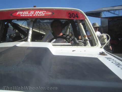 1990 Ford Bronco - driver sits in the caged cockpit of off-road race truck #304, seen through the windshield with a Phils Inc Truck Stuff decal on the cowl.