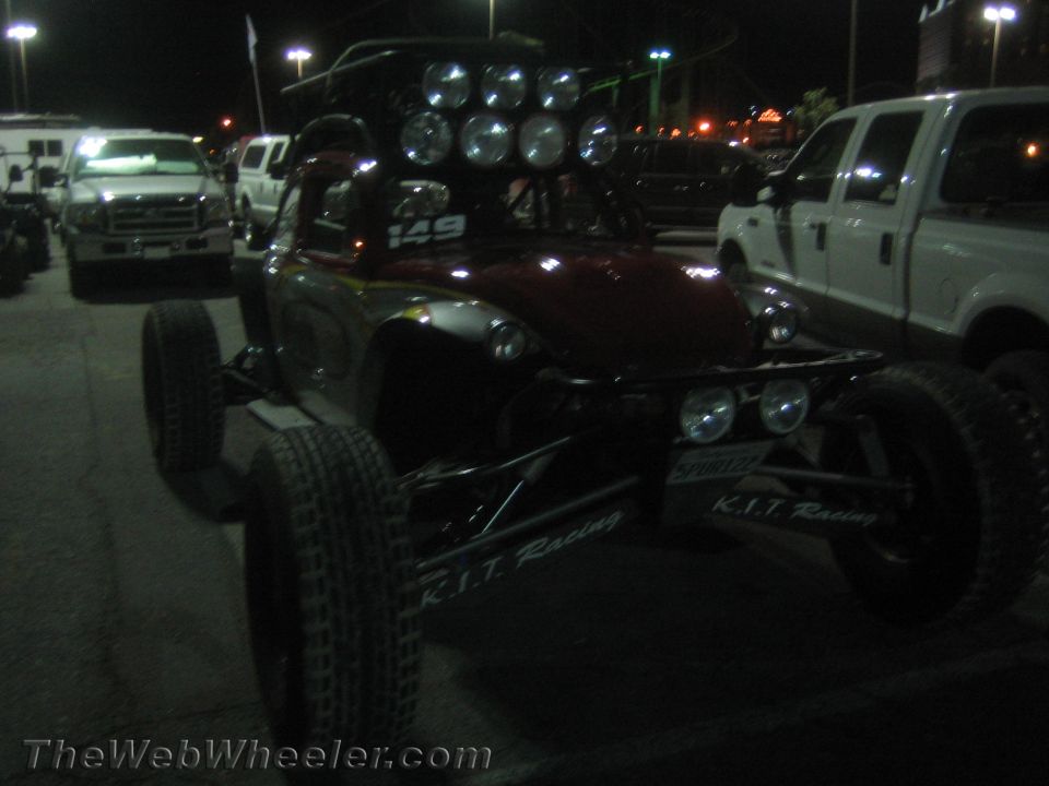 Open off-road race buggy with light bar at night flanked by Ford trucks