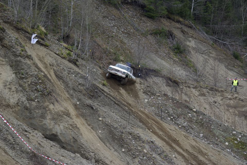 White Jeep Cherokee climbing a steep dirt hill with a person in a yellow vest watching