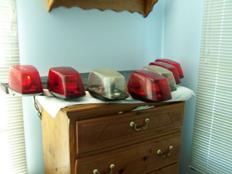 2003 Ford Crown Victoria - A collection of red and clear emergency lights are displayed on top of a wooden dresser.