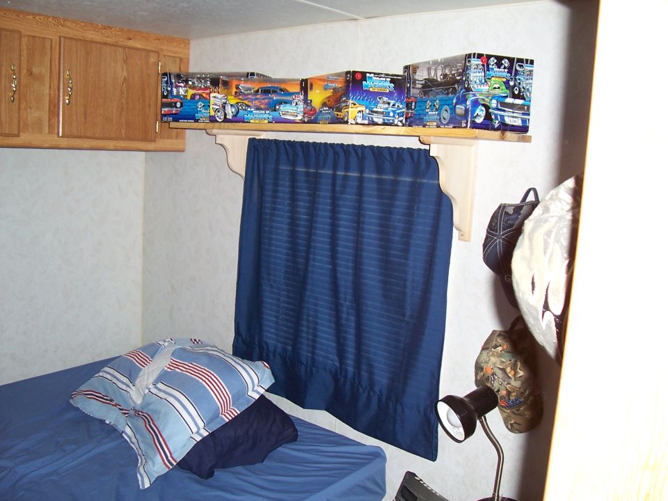 Model car boxes on a shelf above a blue curtain and bed