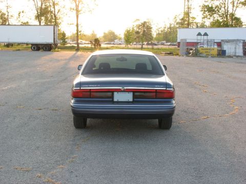 1985 Mercury Grand Marquis - The rear of a blue sedan is shown in a parking lot during sunset.