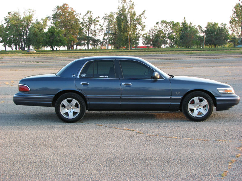 Blue sedan parked on asphalt, side view. Tinted windows, silver alloy wheels