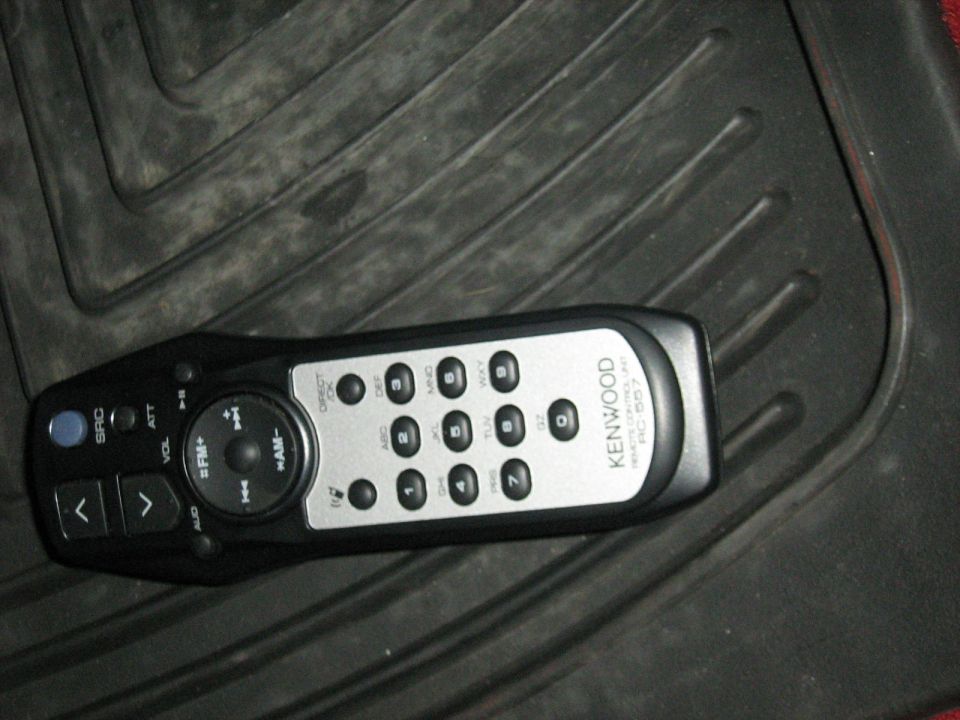 Black and silver Kenwood stereo remote control lying on a rubber floor mat