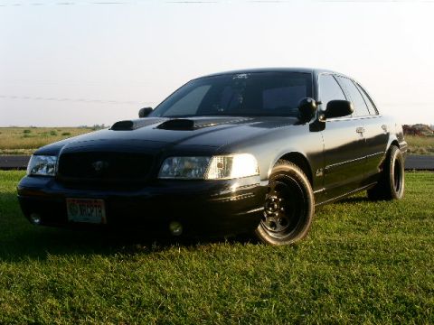 2001 Ford Crown Victoria - This black 2001 Ford Crown Victoria features aftermarket hood scoops and black wheels, seen here parked on a grassy field.