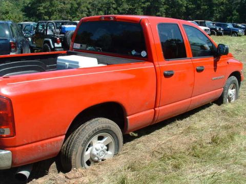 2002 Jeep Wrangler - A red pickup truck is stuck in the mud, with other vehicles visible in the background.