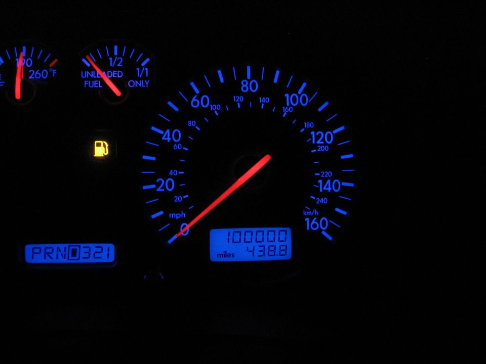 Blue-illuminated VW Jetta gauge cluster showing odometer at 100000 miles with low fuel light on