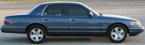 1985 Mercury Grand Marquis - A dark blue sedan is parked outdoors on a paved surface with a blurred background.