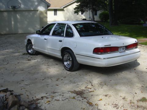 1997 Ford Crown Victoria - A white 1997 Ford Crown Victoria is parked in a residential driveway, showing its rear quarter panel and chrome wheels.