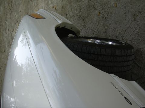 1997 Ford Crown Victoria - Close-up of a white car fender and a spare tire. Text on the fender is visible.
