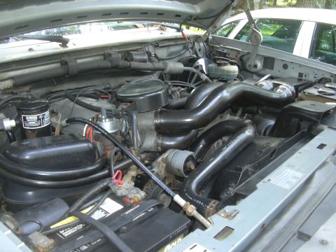 1997 Ford Crown Victoria - The engine bay of a vehicle is shown with prominent black intake hoses and a battery in the foreground.