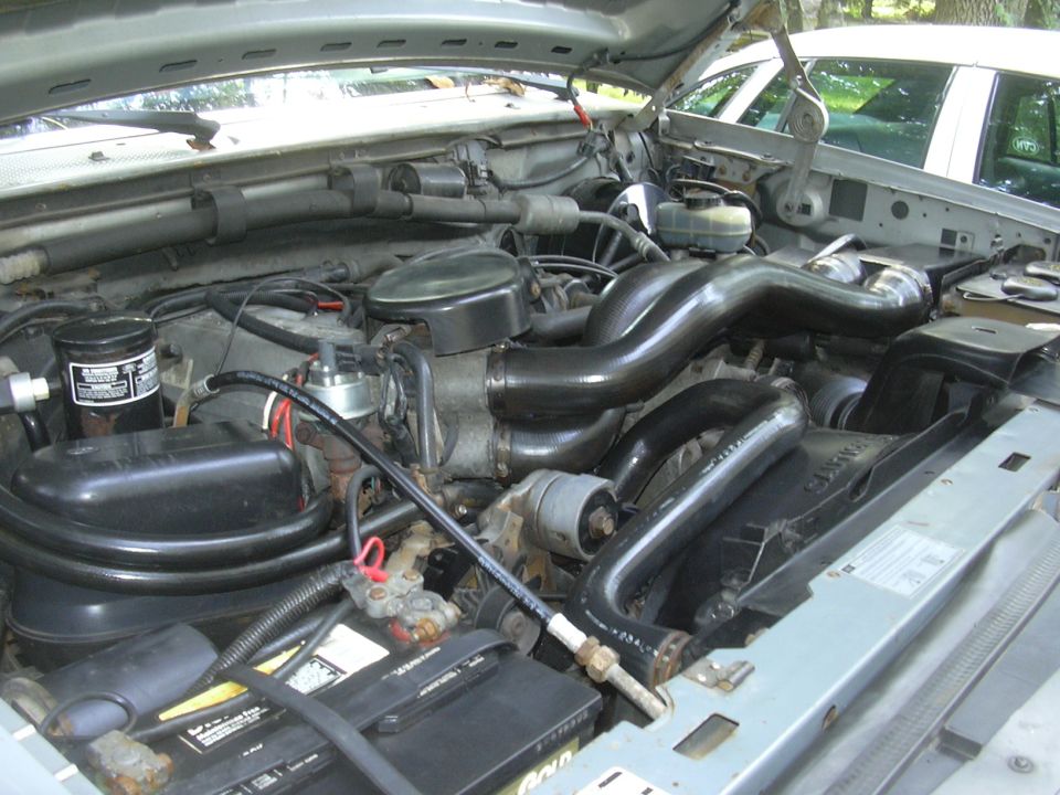 Ford V8 engine bay with hood up showing black intake ducting, battery and master cylinder
