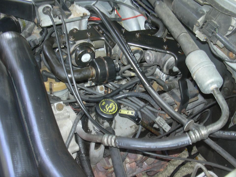 Engine bay with hoses, wires, and engine components visible. Black intake tubes on the left
