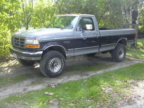 1997 Ford Crown Victoria - A two-tone Ford F-250 pickup truck is parked on a dirt driveway surrounded by trees.