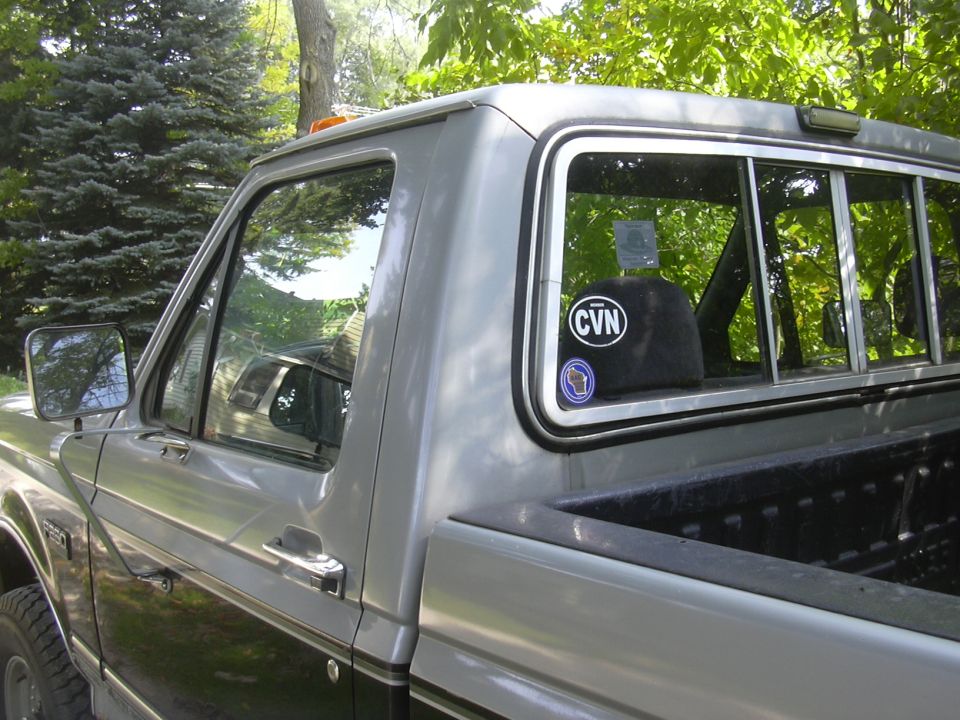 Silver and black pickup truck side view, showing door handle, side mirror, and rear window with stickers