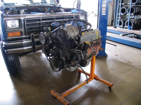 1984 Ford Bronco - Engine removed from a blue Ford Bronco, displayed on an orange stand in a garage.