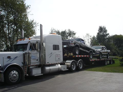 1979 Ford Bronco - A semi-truck transports two pickup trucks on its trailer, a load of vehicles.