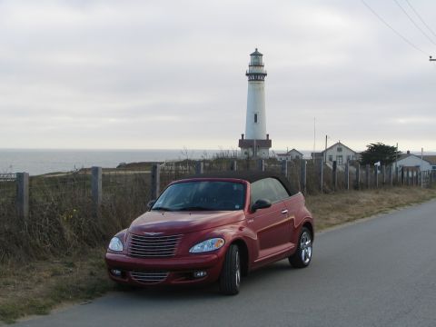 2005 Chrysler PT Cruiser - A red 2005 Chrysler PT Cruiser convertible is parked on the side of a road with a lighthouse and the ocean in the background.