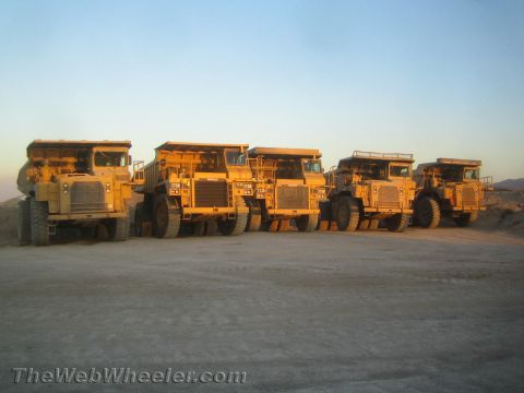 1968 Ford Mustang - Several large yellow mining dump trucks are lined up in an outdoor lot under a clear sky.