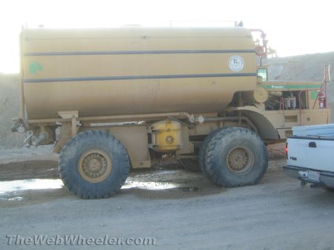 1968 Ford Mustang - A large, industrial water truck with a massive tank sits on a dirt road, partially obscured by a pickup truck.