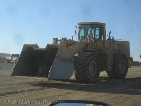 1968 Ford Mustang - A large yellow wheel loader sits in a dirt lot under a clear blue sky.