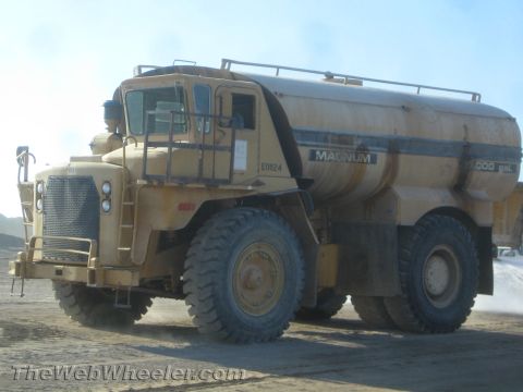 1968 Ford Mustang - A large yellow water truck with dual rear wheels is seen in a dusty outdoor environment.