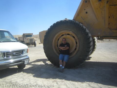 1968 Ford Mustang - A person stands next to an enormous tire, dwarfed by the scale of heavy construction equipment in a dusty outdoor setting.