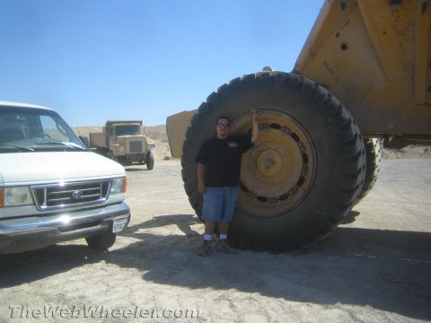 1968 Ford Mustang - A person stands next to the enormous tire of a mining truck, with a white van and a dump truck visible in the background.