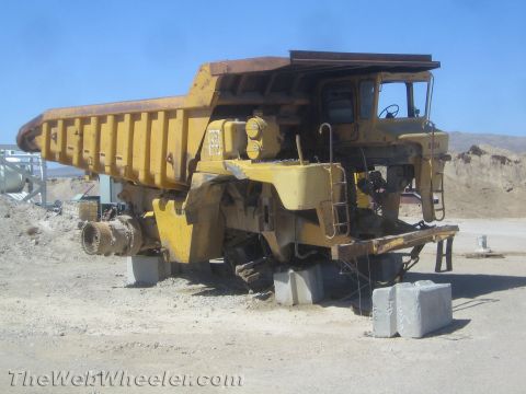 1968 Ford Mustang - A large yellow mining dump truck is parked on concrete blocks in an outdoor industrial area.