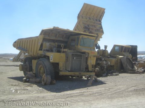 1968 Ford Mustang - Two yellow dump trucks are parked in a lot under a clear blue sky, one with its bed raised.