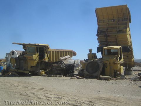 1968 Ford Mustang - Two large yellow dump trucks sit in a dusty lot under a bright blue sky, appearing to be in a state of disrepair.
