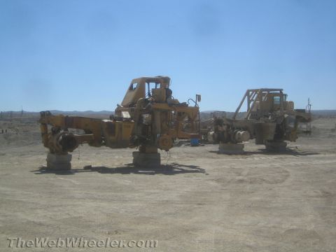 1968 Ford Mustang - Two unfinished chassis of heavy construction equipment sit on concrete blocks under a clear blue sky.