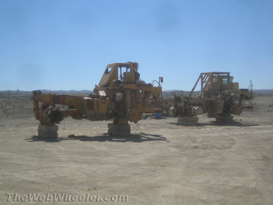 two yellow heavy equipment chassis on concrete blocks in a dusty lot