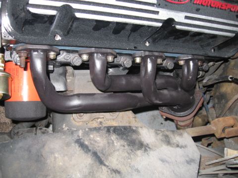 1988 Mercury Grand Marquis - Close-up view of an engine's exhaust manifold with black headers and an orange oil filter visible.