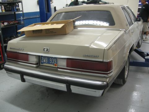 1988 Mercury Grand Marquis - A tan 1988 Mercury Grand Marquis is shown from the rear, elevated on a lift in a garage.