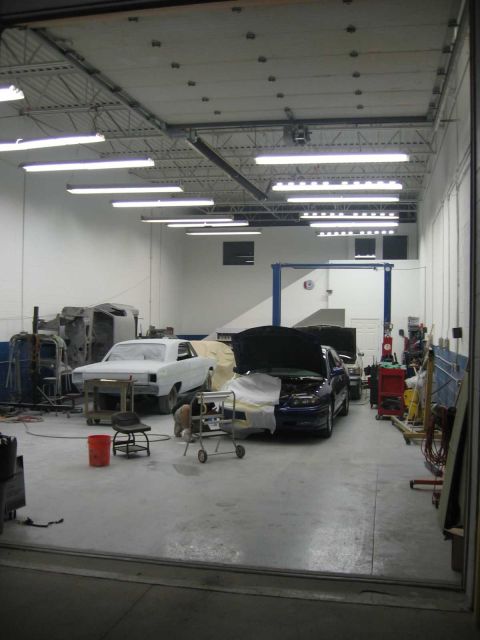 1988 Mercury Grand Marquis - An auto repair shop interior with two vehicles undergoing work, one covered and one with its hood open.