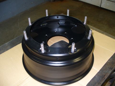 1978 Ford Bronco - A black steel wheel rim with six lug studs is shown, resting on cardboard.