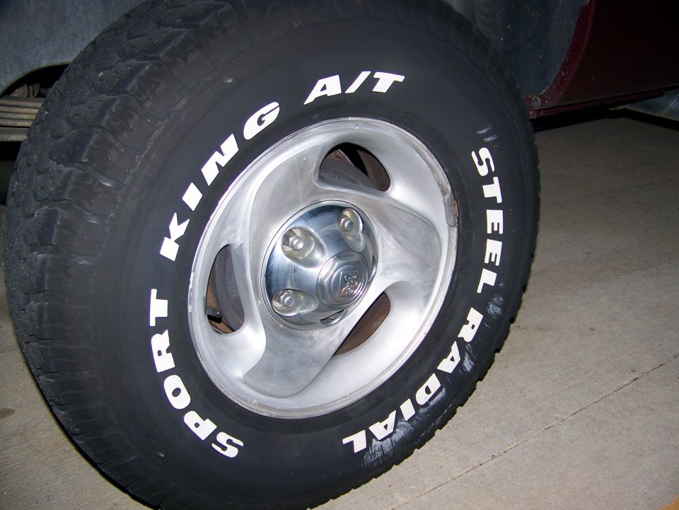 Close-up of a truck wheel with 'SPORT KING A/T' and 'STEEL RADIAL' tire lettering. The wheel has five lug nuts